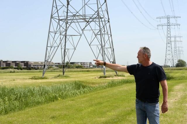 Bewoner wijst naar een bestaande hoogspanningsmast bij de woonwijk