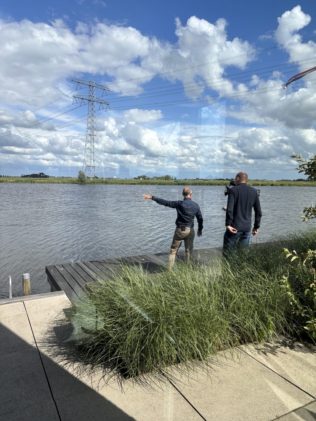 Bewoner wijst over het water naar het tracé van de geplande hoogspanningsverbinding bij Leeuwarden